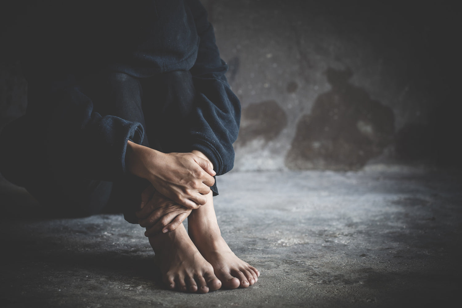 Person sitzt mit angezogenen Beinen auf kaltem Boden, wirkt erschöpft und zurückgezogen – symbolisch für Einsamkeit, Verzweiflung und die emotionale Last einer Cannabis-Abhängigkeit.