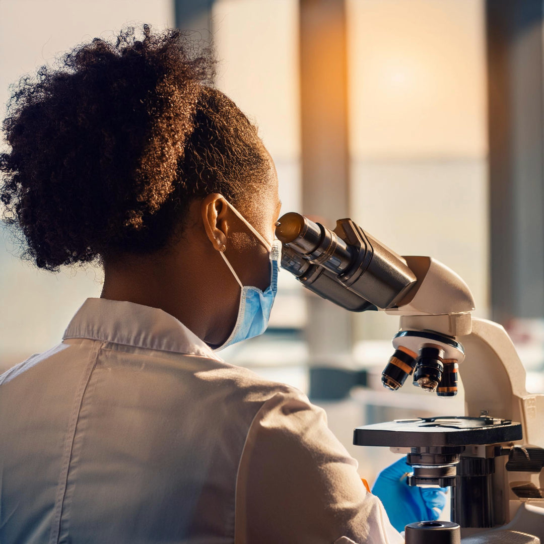 Eine Wissenschaftlerin in einem Laborkittel schaut durch ein Mikroskop und analysiert Proben.