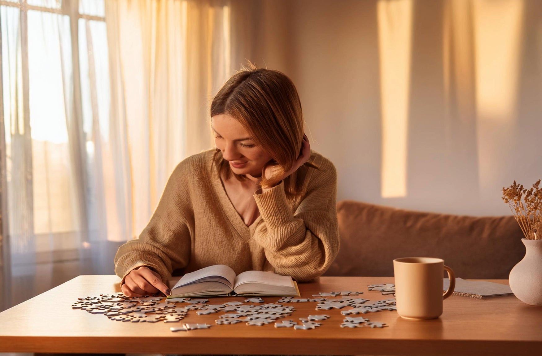 Eine Frau sitzt an einem Tisch, betrachtet ein Puzzlestück und arbeitet an einem Puzzle, das vor ihr liegt. Nebenbei versucht sie noch ein Buch zu lesen.