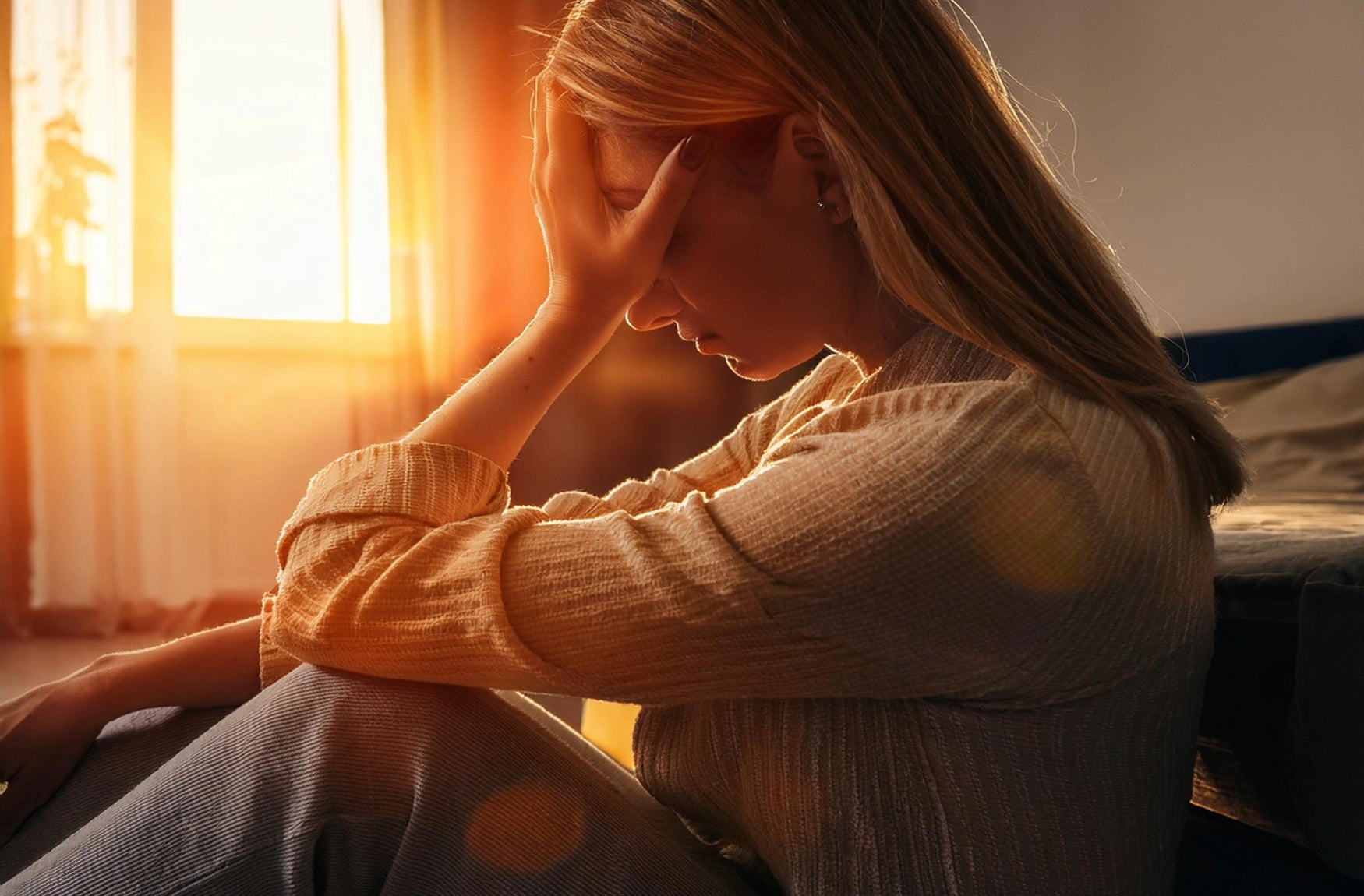 Eine Frau sitzt auf dem Boden und hält ihren Kopf in den Händen, sichtbar in Gedanken versunken oder verzweifelt.