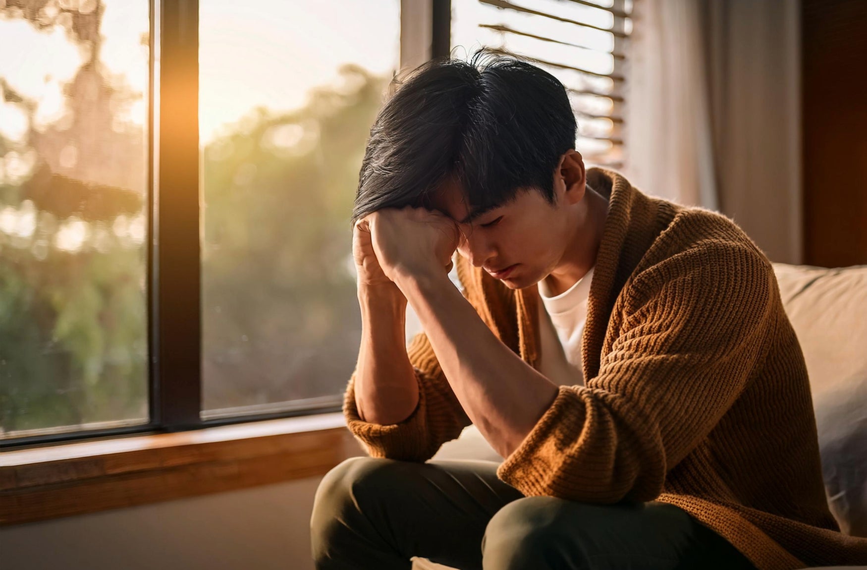 Ein Mann sitzt auf einer Couch und hält seinen Kopf in seinen Händen, sichtbar in Gedanken versunken.