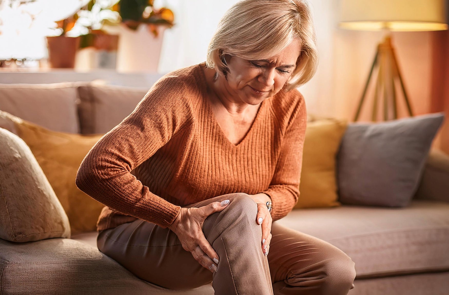 Eine Frau sitzt auf einem Sofa und hält sich schmerzhaft ihr Knie.